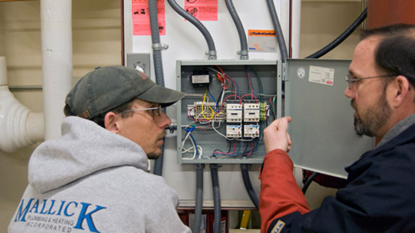 Two men looking over and discussing a fusebox.